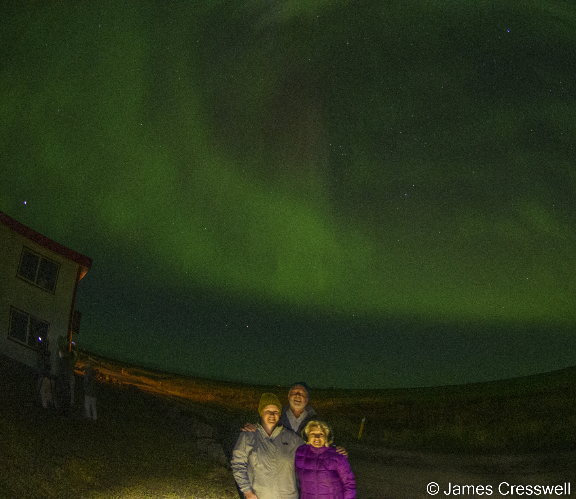 Three people outside at night under the Northern Lights